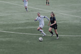 Two female soccer players on a field with one controlling the ball.